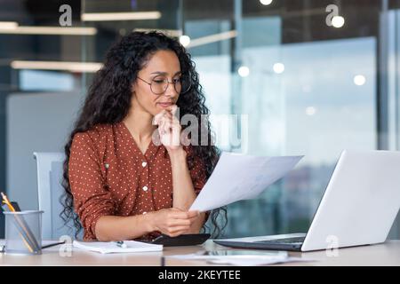 Successful satisfied and happy business woman working inside modern office, hispanic woman in glasses and shirt using laptop at work, Stock Photo