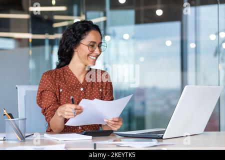 Successful satisfied and happy business woman working inside modern office, hispanic woman in glasses and shirt using laptop at work, Stock Photo
