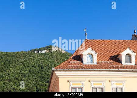 Tiled roof of 17th century Council House against the backdrop of forested hills with giant letters on the top BRASOV, Romania Stock Photo