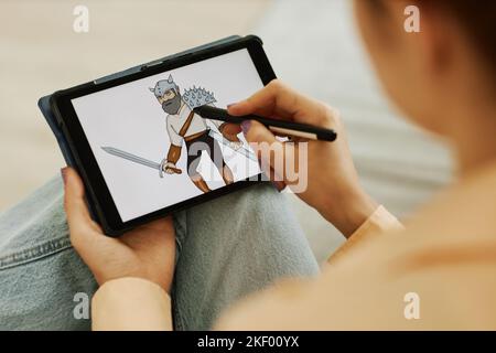 Selective focus on graphic picture of warrior on screen of tablet held by young female digital artist with stylus creating new images Stock Photo