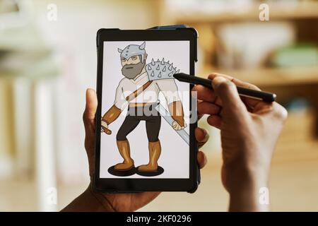 Tablet with graphic image of warrior on screen in hands of African American designer using stylus while creating new picture Stock Photo