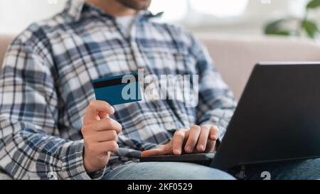 Millennial caucasian man in domestic clothes sit on sofa with computer and credit card shopping online Stock Photo