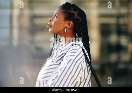 Sideview of a young businesswoman looking thoughtful while standing outdoors in the city. Young black business woman commuting to work in the morning. Stock Photo