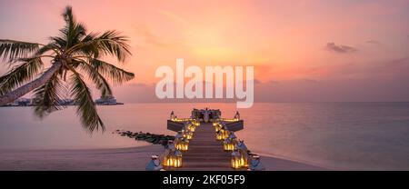 Romantic dinner on the beach with sunset, candles with palm leaves and sunset sky and sea. Amazing view, honeymoon or anniversary dinner landscape Stock Photo