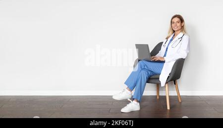 Medical Banner. Smiling Doctor Lady Using Laptop While Sitting On Chair Stock Photo