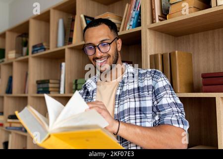 Arab male student reading book and learning while sitting in university library indoors, copy space Stock Photo