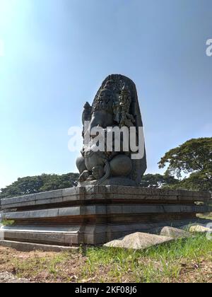 A majestic stone sculpture of Lord Ganesha, intricately carved with a large head and crown, holds an axe and modak. Seated against a clear sky. Stock Photo