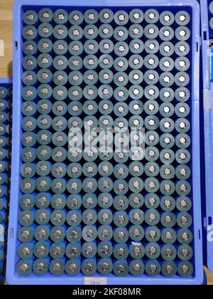 A top-down view of a blue plastic tray filled with cylindrical lithium-ion batteries arranged in a neat grid. Each silver-cased battery. Stock Photo