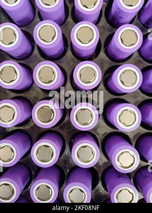 A closeup of neatly arranged cylindrical lithium-ion batteries in a vibrant purple with a metallic finish. Stock Photo