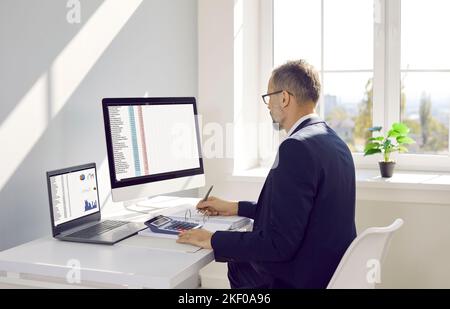 Business accountant sitting at office desk and working on desktop and laptop computers Stock Photo