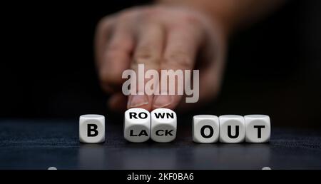 Hand turns dice and changes the expression 'blackout' to 'brownout'. Stock Photo