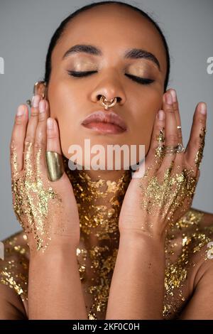 Portrait of stylish african american woman with golden foil on chest and hands isolated on grey,stock image Stock Photo