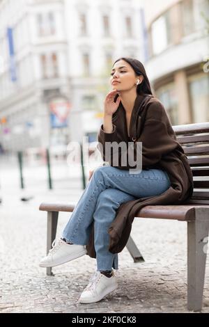 dreamy woman sitting on bench in prague and listening music in wireless earphone,stock image Stock Photo