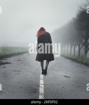 Young woman with red hair walking down an empty road in the mist Stock Photo