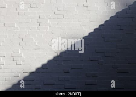 White brick wall is divided into light and shadow parts along the diagonal in form of steps. White and Black. Background. Texture. Free space for text Stock Photo