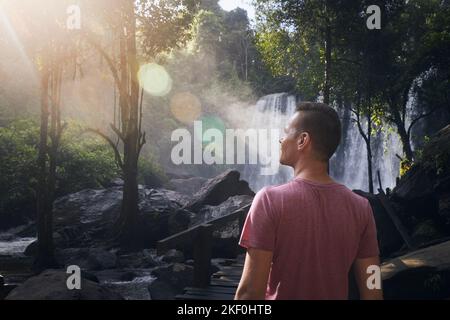 Man walking through rainforest to high waterfall in mountains. Tourist enjoying tropical nature in Camobodia. Stock Photo