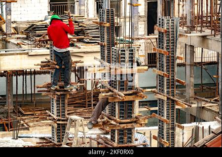 A construction worker nails wood poles as temporary supports to steel formwork for concrete columns. Stock Photo