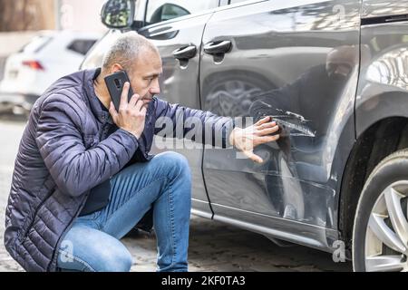 A man calls the insurance company or the police because someone backed into the side door of his car in the parking lot. Stock Photo