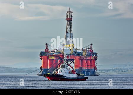 Cromarty Firth Scotland tug boat Strathdon sailing in front of the orange oil rig Transocean Leader Stock Photo