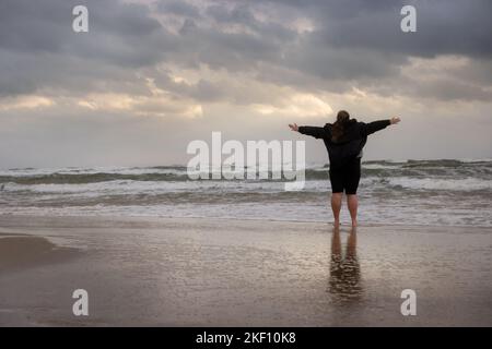 Person standing on the beach on the cloudy day. Sea shore after the storm with the woman looking at the horizon. Stock Photo