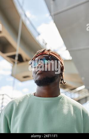Vertical portrait of young black man wearing street style clothes looking up confidently in urban setting Stock Photo