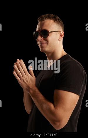 Portrait of stylish , brutal, young man posing in trendy sunglasses isolated over black studio background. Concept of fashion and lifestyle Stock Photo