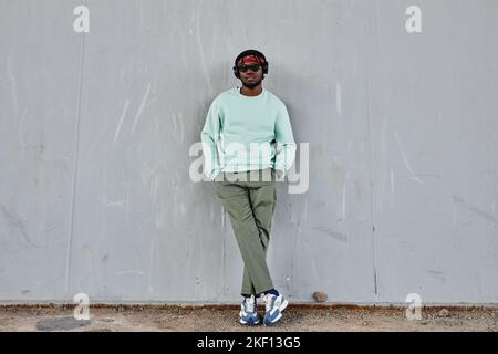 Minimal full length portrait of young black man wearing street style clothes leaning on concrete wall outdoors, copy space Stock Photo