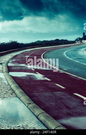 Cycling path hugging the Cascais, Portugal coast on a rainy day on a dark autumn day Stock Photo