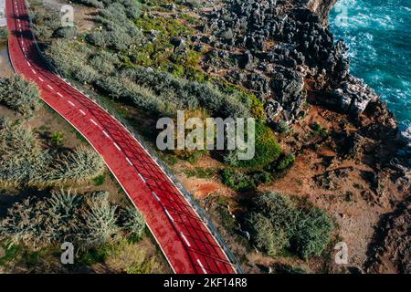 Aerial drone view of red cycling path hugging the Cascais, Portugal coast on a sunny day Stock Photo
