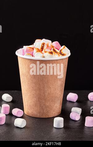 Paper cup with hot drink with marshmallows on dark background. Stock Photo