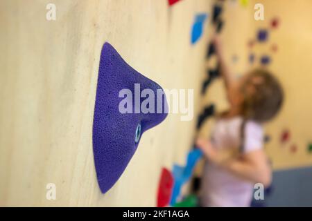 Selective focus on artificial bouldering stone. Girl child do bouldering known as free climbing exercise indoors leisure activity. Stock Photo