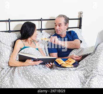 Mature couple in bed, eating breakfast Stock Photo