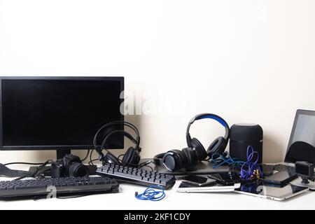 Old computers, digital tablets, mobile phones, headphones, many used electronic gadgets devices on white table. E-waste, planned obsolescence Stock Photo