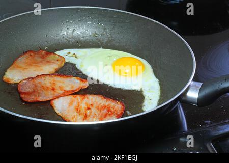 Egg and three rashers of bacon being fried in a frying pan for breakfast. Stock Photo