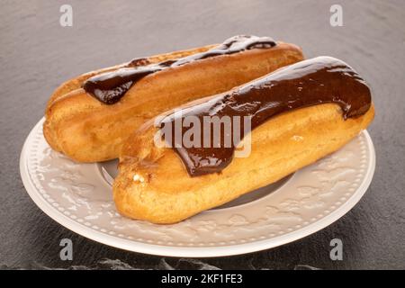 Two sweet eclairs with white plate on slate stone, macro. Stock Photo