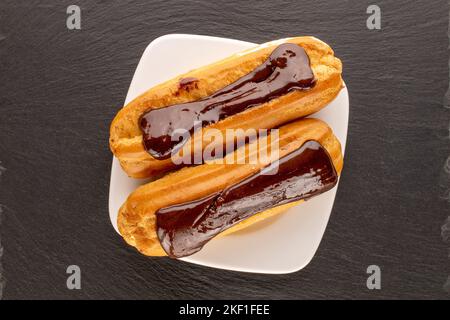 Two sweet eclairs with white plate on slate stone, macro, top view. Stock Photo