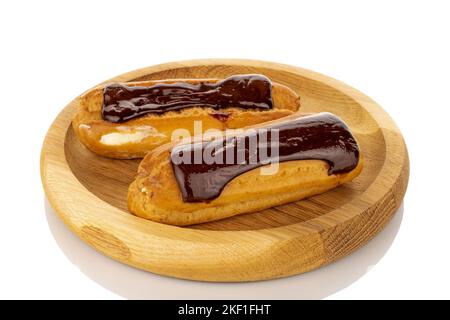 Two sweet chocolate eclairs on a wooden plate, macro, isolated on white background. Stock Photo