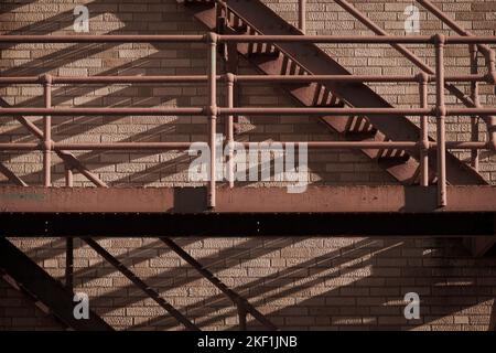 Red painted tubular metal fire escsape on side of brick building. Stock Photo