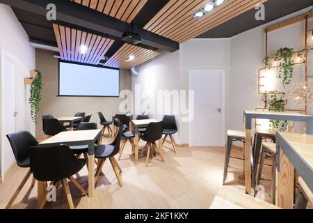 A restaurant room with tall wooden tables and chairs and a copper shelf with artificial plants and a tv screen on the wall Stock Photo