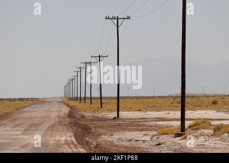 Lonely empty gravel road with poles stretching for miles into the desert