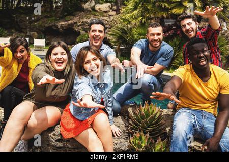 Joyful multiethnic diverse group of young people having fun together posing looking at the camera with arms outstretched - happy people lifestyle conc Stock Photo