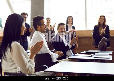 Business people applaud and cheers man on business meeting or training in bright modern office. Stock Photo