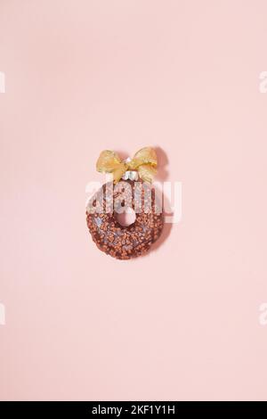 chocolate donut with golden bow on pink background. single glazed ball top view Stock Photo