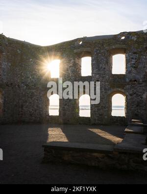 A sun shining through one of the six window openings on a wall of the crumbling Brahehus Castle and a view of calm sea and clear sky Stock Photo