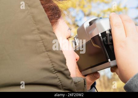 Side view photo of a photographer woman outdoors holding camera close to her face and taking photo of a beautiful winter nature. Stock Photo