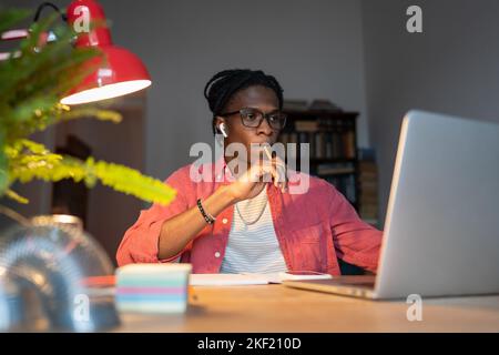 Concentrated pensive African American man student looks at laptop sits at computer in home office Stock Photo