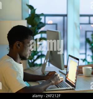 Concentrated African American man student typing email on laptop keyboard sits at office table desk. Stock Photo