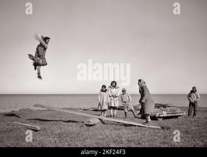 1950s INUIT NATIVE AMERICAN INDIAN ADULTS TEENS KIDS PLAYING A SEESAW TOSS JUMPBOARD WITH ONE GIRL UP IN THE AIR KOTZEBUE ALASKA - c2683 BAU001 HARS NOSTALGIC PAIR COMMUNITY OLD TIME NOSTALGIA OLD FASHION 1 JUVENILE STYLE TEAMWORK JOY LIFESTYLE SATISFACTION FEMALES ESKIMO RURAL HEALTHINESS HOME LIFE 6 UNITED STATES COPY SPACE FRIENDSHIP FULL-LENGTH LADIES PERSONS SEESAW INDIANS UNITED STATES OF AMERICA MALES SIX B&W NORTH AMERICA NORTH AMERICAN ALASKA HAPPINESS ADVENTURE LEISURE AND EXCITEMENT UP INUIT CULTURE TEENAGED KOTZEBUE NATIVE AMERICAN ARCTIC COOPERATION GROWTH NATIVE AMERICANS Stock Photo