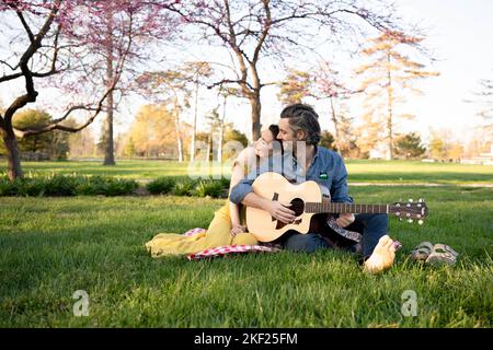 Couple in love on a picnic in Forest Park. The man is playing a guitar for his woman. Stock Photo