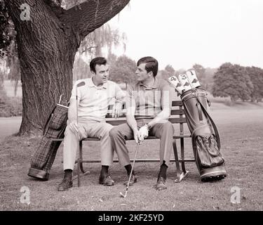 1960s TWO MEN SITTING ON GOLF COURSE BENCH UNDER A TREE CHATTING TALKING HOLDING IRONS - g7201 HAR001 HARS GOLFERS LEISURE NETWORKING BONDING RECREATION COUNTRY CLUB BUSYBODY TELLING OPPORTUNITY TO MASCULINE STORIES CONNECTION FRIENDLY LINKS MALE BONDING TATTLER HEARSAY COOPERATION GOLF BAGS MID-ADULT MID-ADULT MAN RUMORS TOGETHERNESS BLACK AND WHITE CAUCASIAN ETHNICITY HAR001 OLD FASHIONED Stock Photo